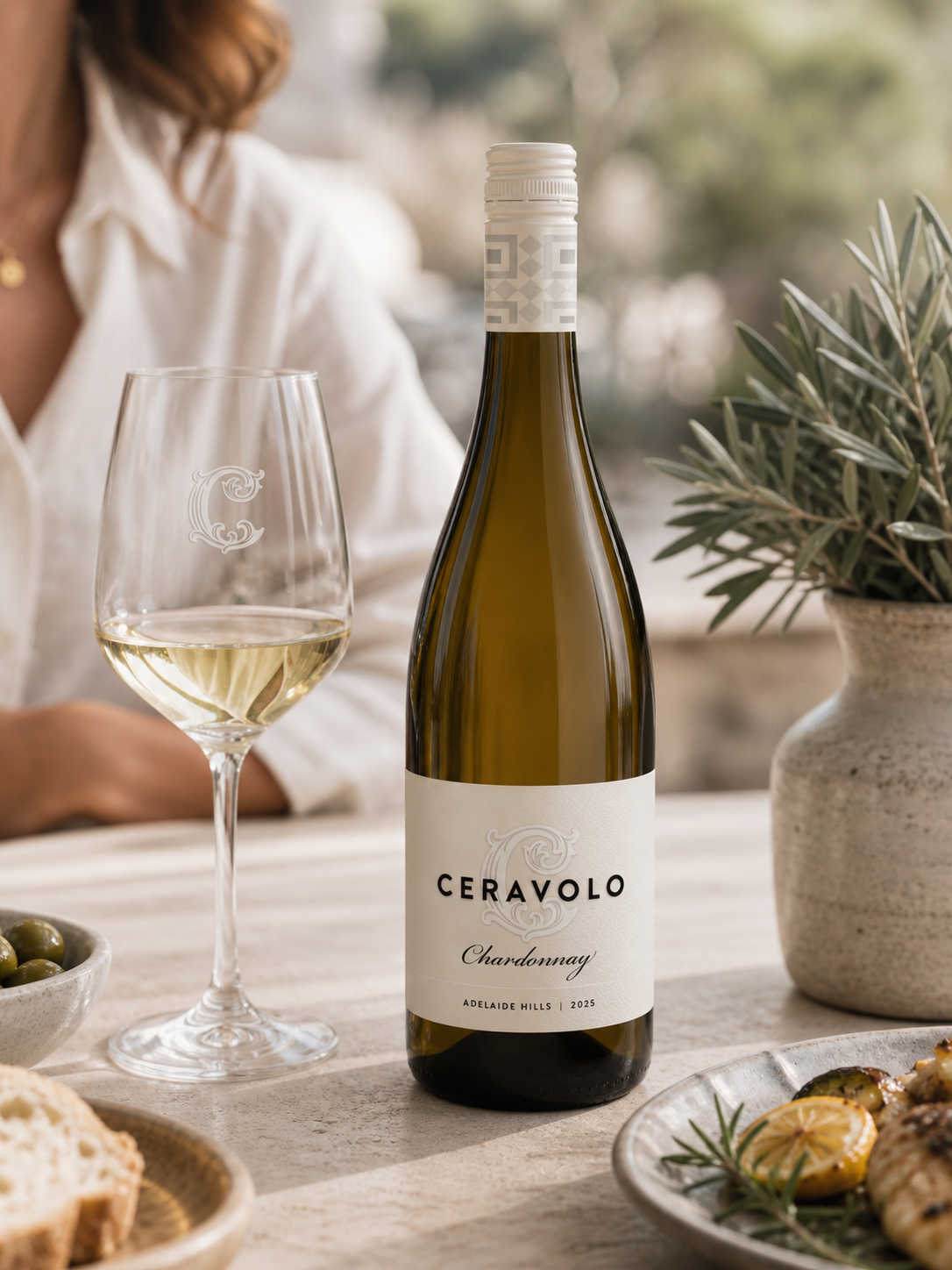 Glass of Ceravolo Chardonnay with food on a table with rosemary.